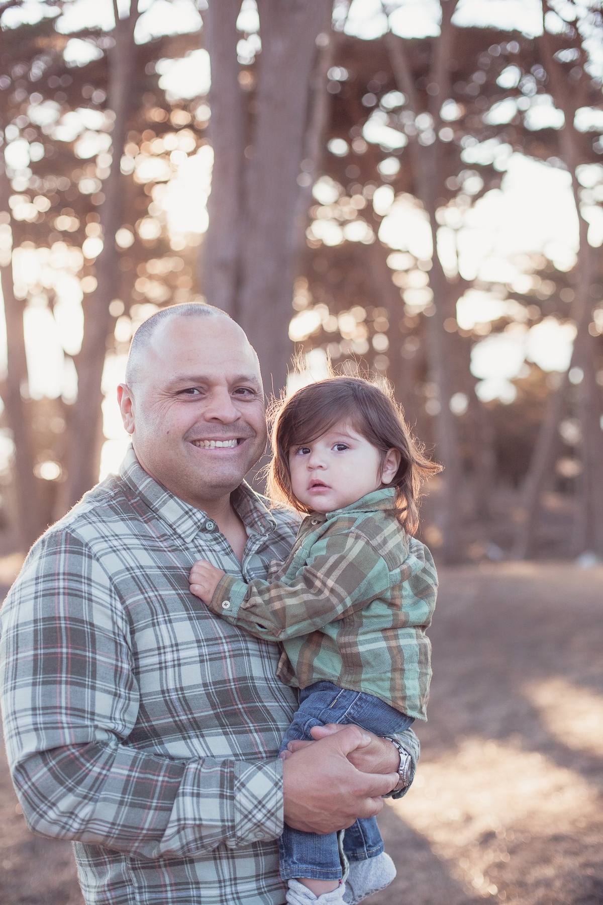 Father in a plaid shirt holding his toddler son in matching plaid among the cypress trees