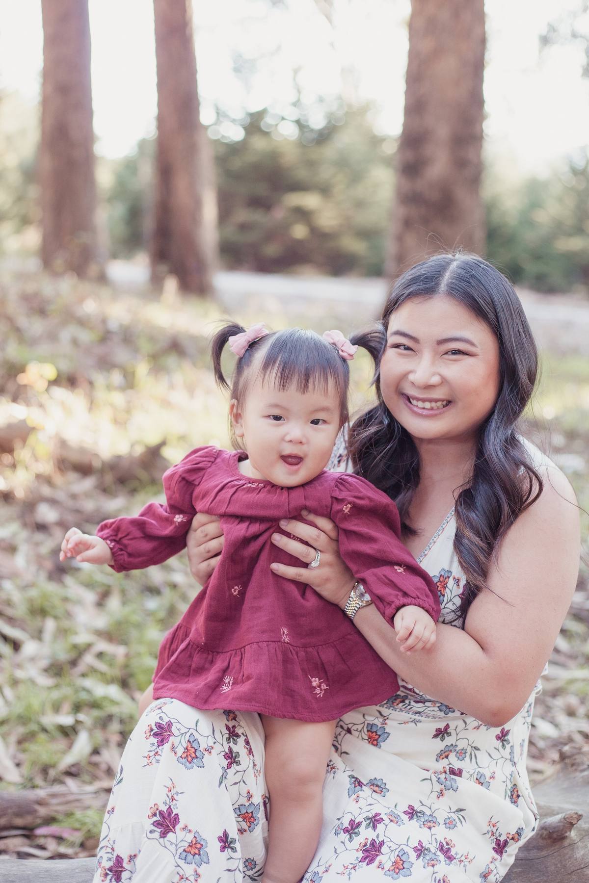Baby girl in a burgundy dress laughing in her mother's arms at Wood Line