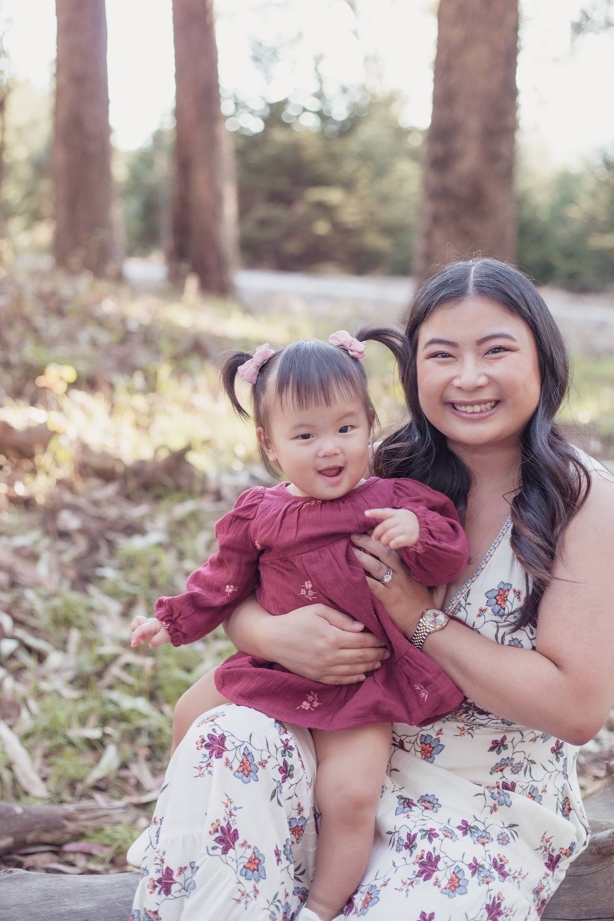 Mother holding her baby daughter on her lap in the warm light of the eucalyptus grove