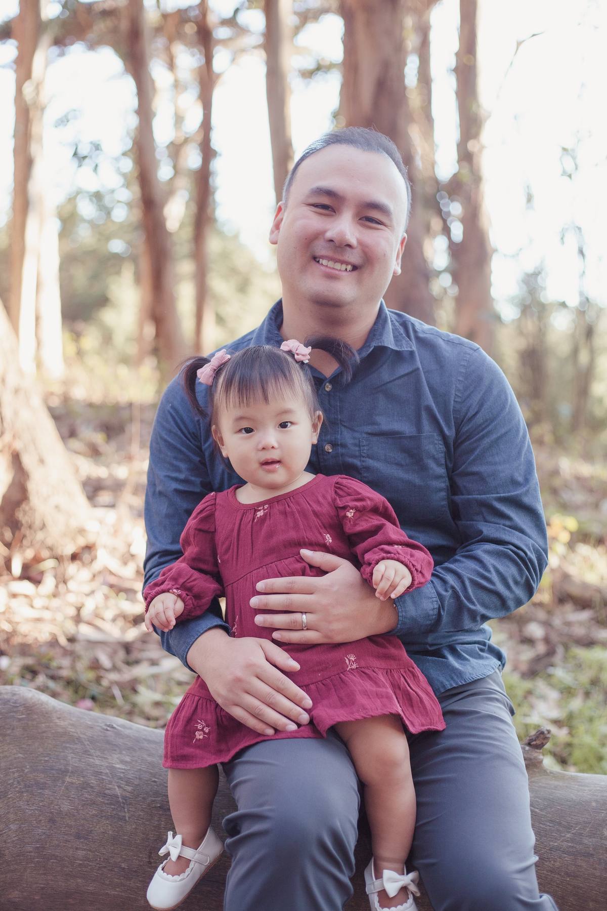 Father holding his baby girl on a log among the eucalyptus trees in the Presidio