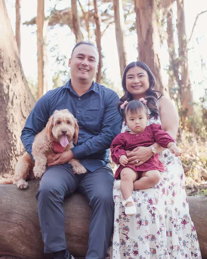Parents, baby girl, and their dog sitting on a log at Andy Goldsworthy's Wood Line