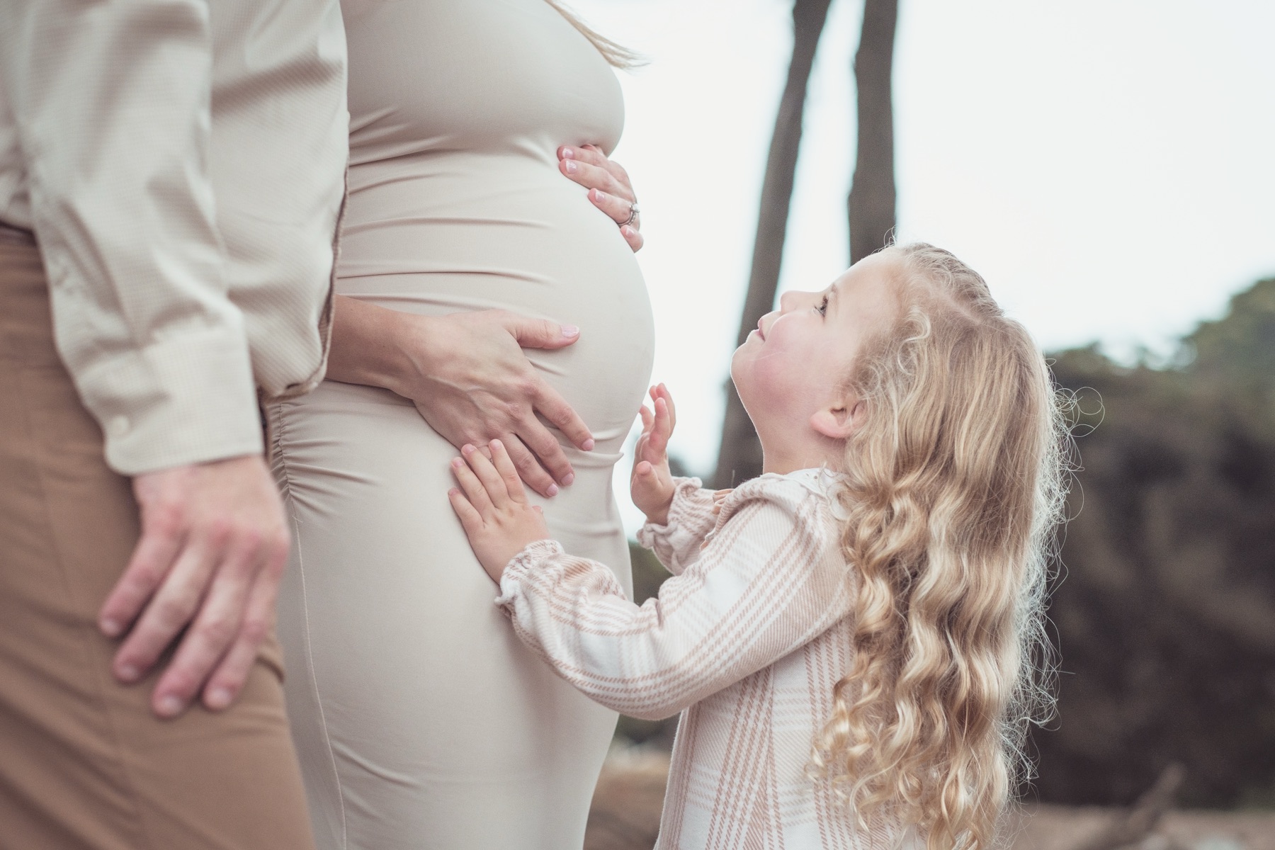 Toddler reaching for her mother's pregnant belly outdoors