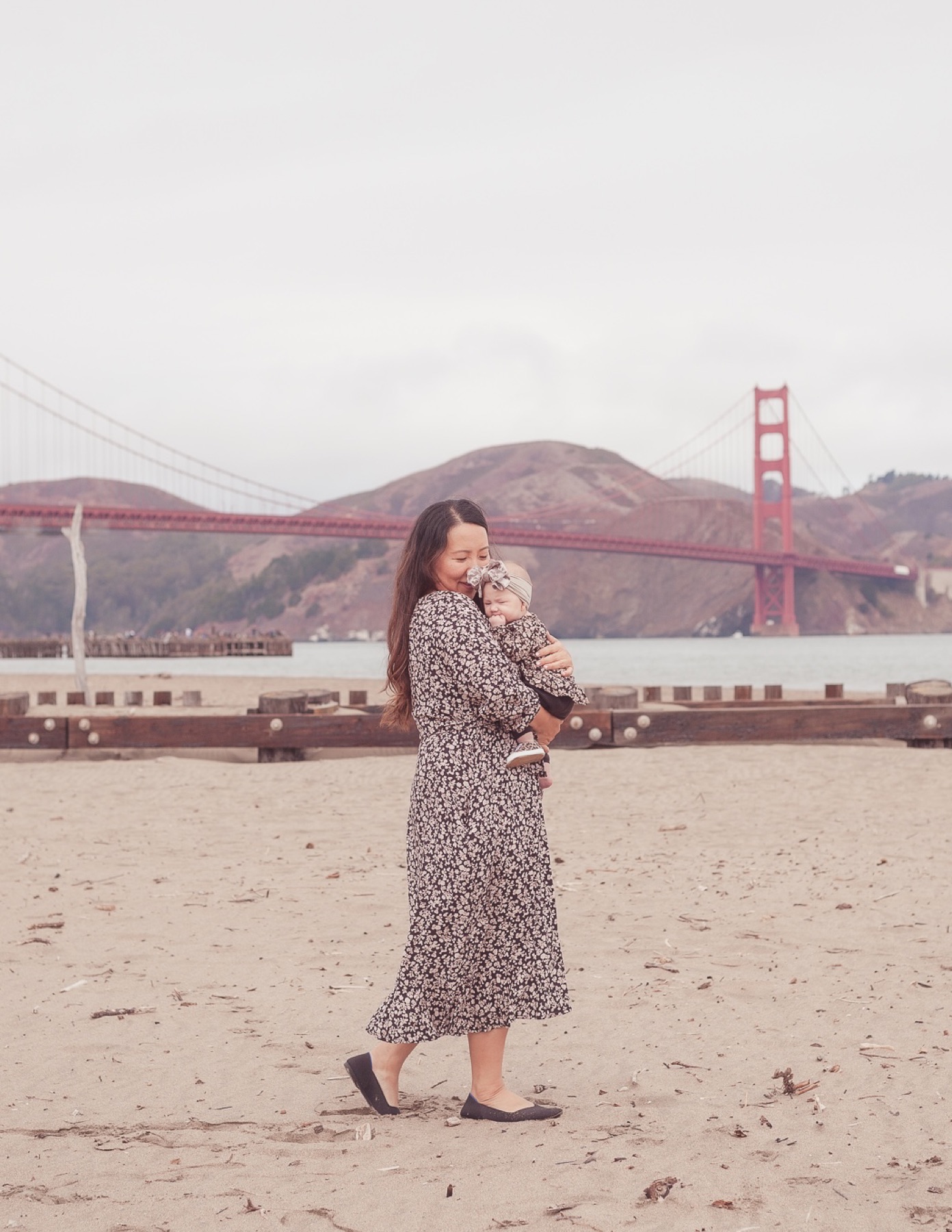 Mother holding her baby on the beach near the Golden Gate Bridge