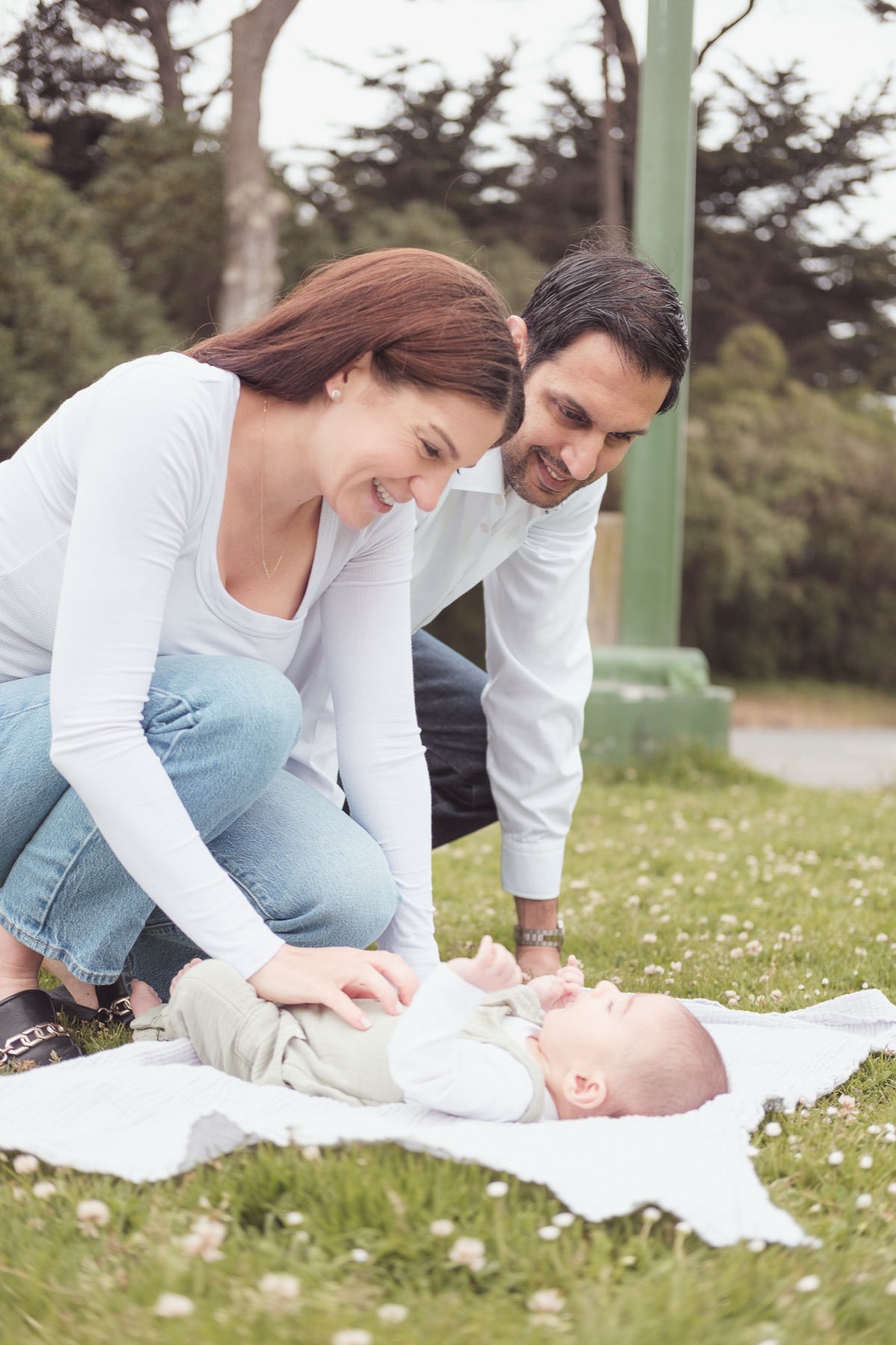Parents smiling at their newborn on a blanket in the grass