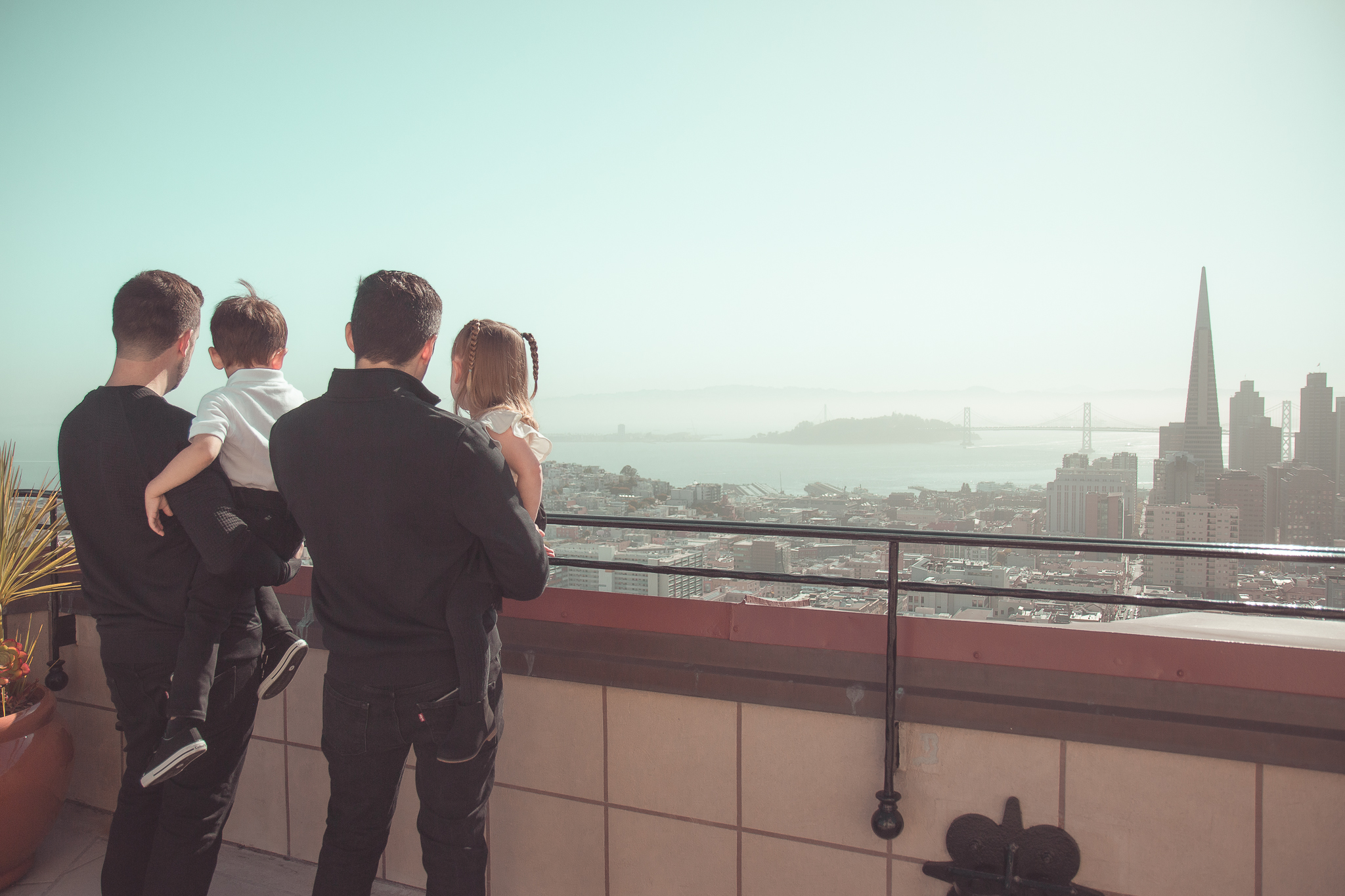 Two dads holding their kids while looking out at the San Francisco skyline