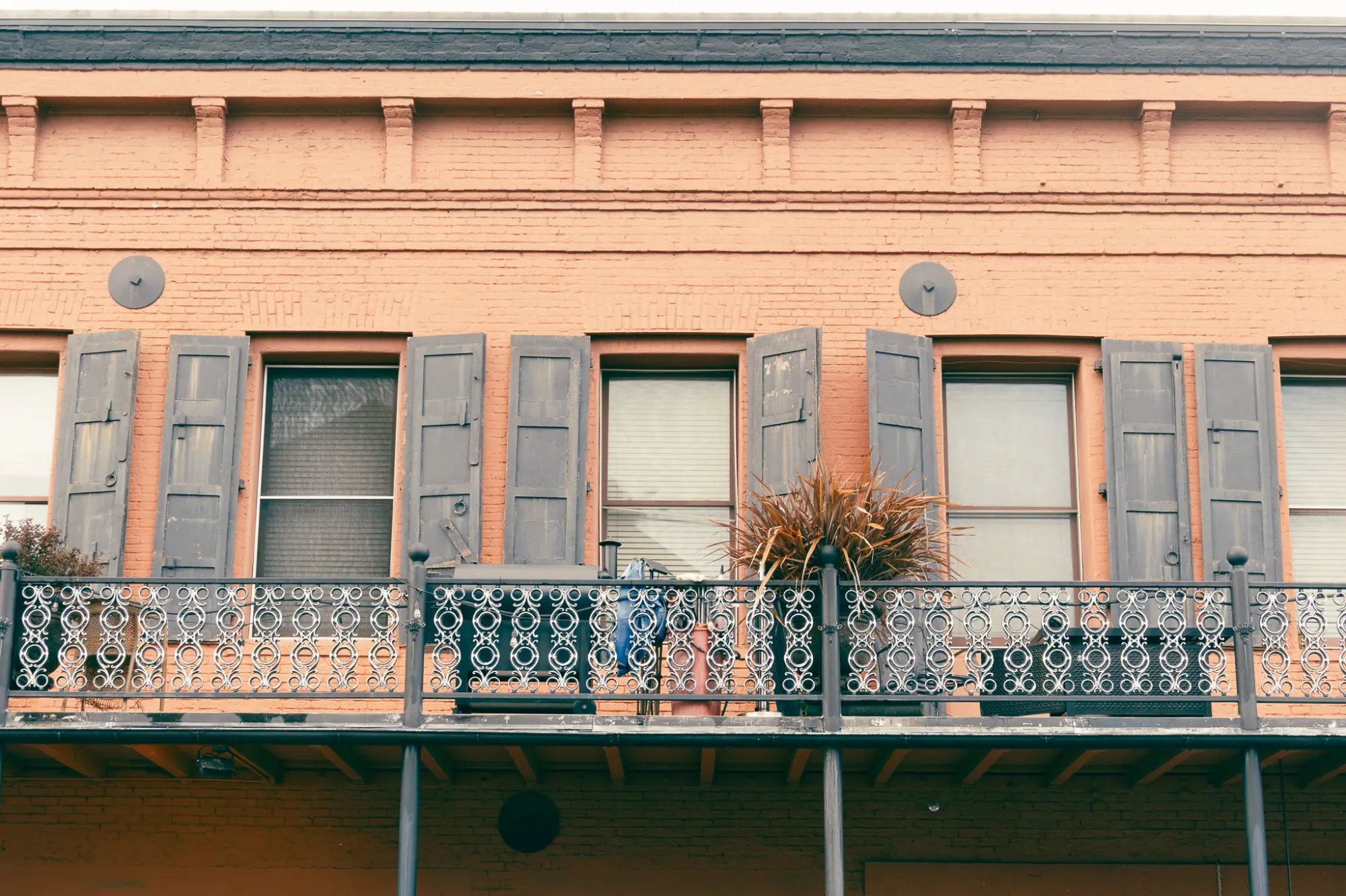 A brick facade with shutters and a wrought-iron balcony