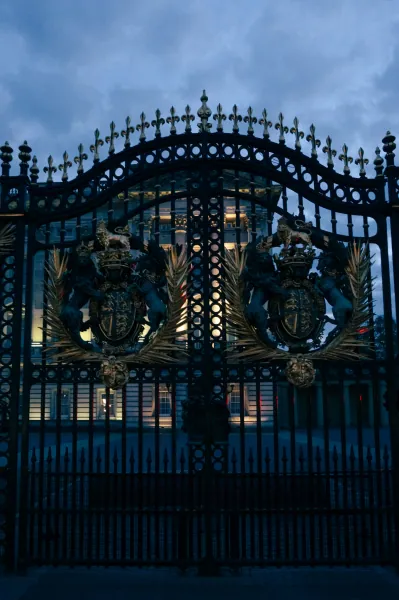 Ornate black-and-gold gates with royal coat of arms at dusk