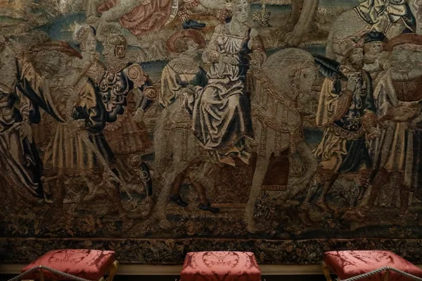 Large figurative tapestry above red stools