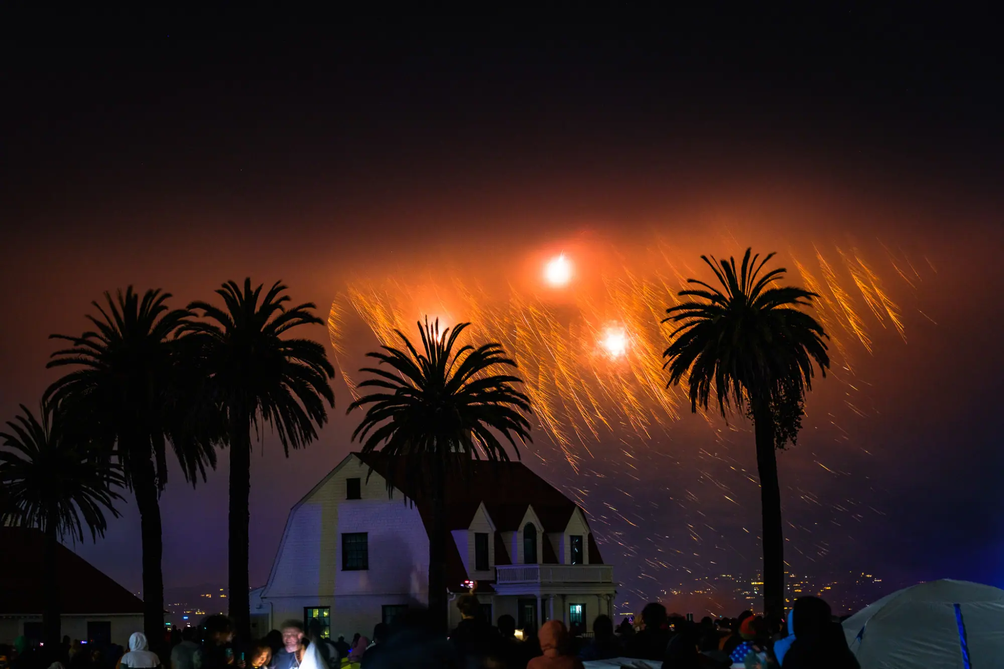 Orange bursts in the fog above the palms and the crowd